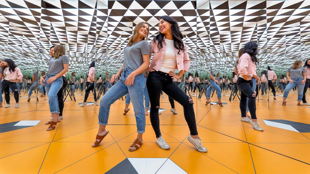 Two beautiful ladies are taking pictures in a room with lots of mirrors.